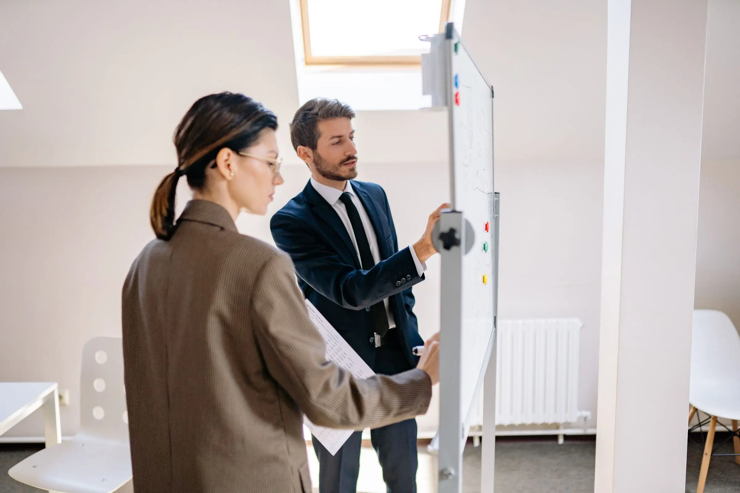 Two colleagues discussing a plan on a whiteboard